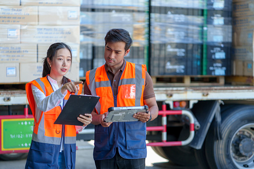 Shift workers in hi-vis vests reviewing a timesheet on a tablet beside a delivery truck